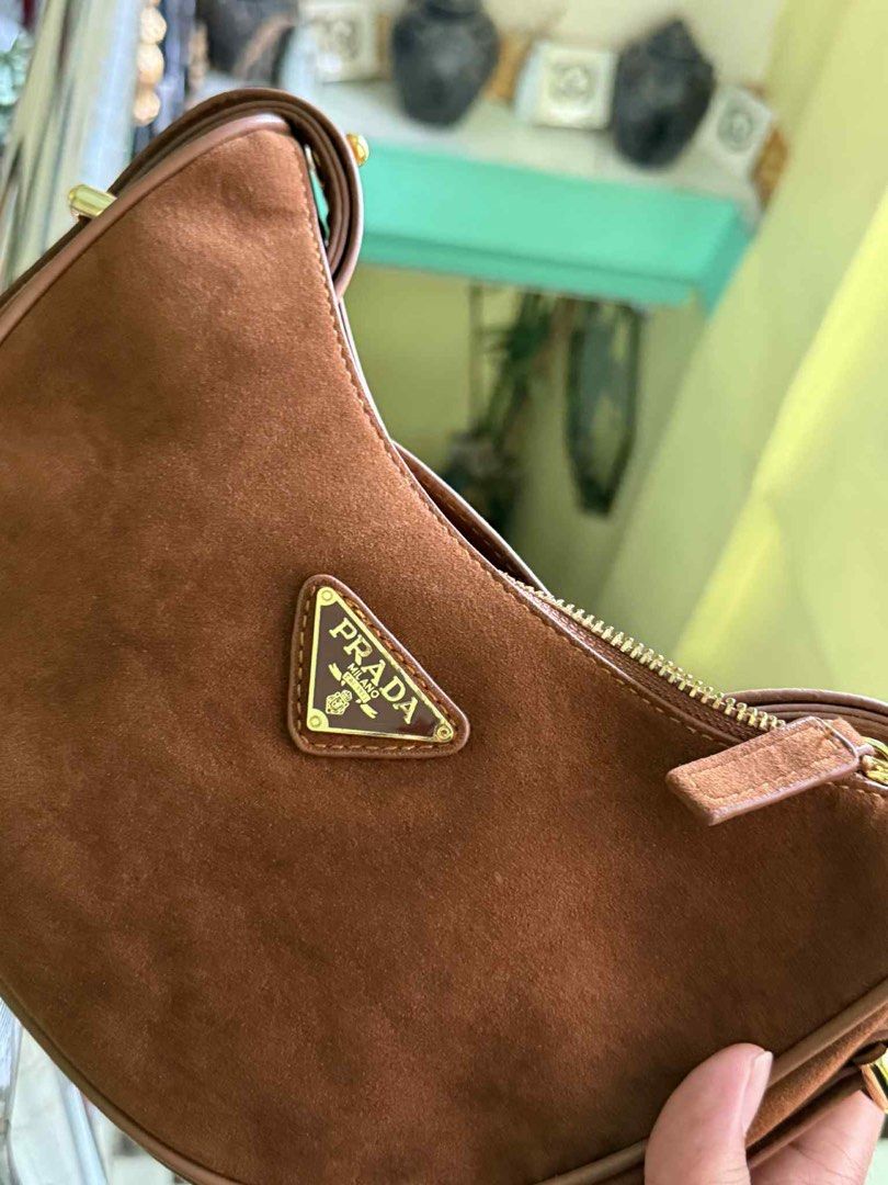 Prada Arque Suede Bag (Category: Luxury Bags & Wallets) located in Cabuyao City. Submitted by girliecloset202434 (Listing ID 1427527811, Image 3). Description: Brown suede Prada hobo bag. Features a gold-tone zipper and a triangular Prada logo on the front. The interior has a Prada label. Includes a Prada dust bag. The bag has a curved shape and a single shoulder strap..