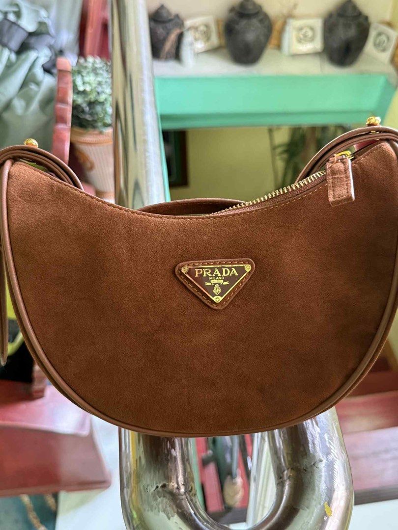 Prada Arque Suede Bag (Category: Luxury Bags & Wallets) located in Cabuyao City. Submitted by girliecloset202434 (Listing ID 1427527811, Image 1). Description: Brown suede Prada hobo bag. Features a gold-tone zipper and a triangular Prada logo on the front. The interior has a Prada label. Includes a Prada dust bag. The bag has a curved shape and a single shoulder strap..