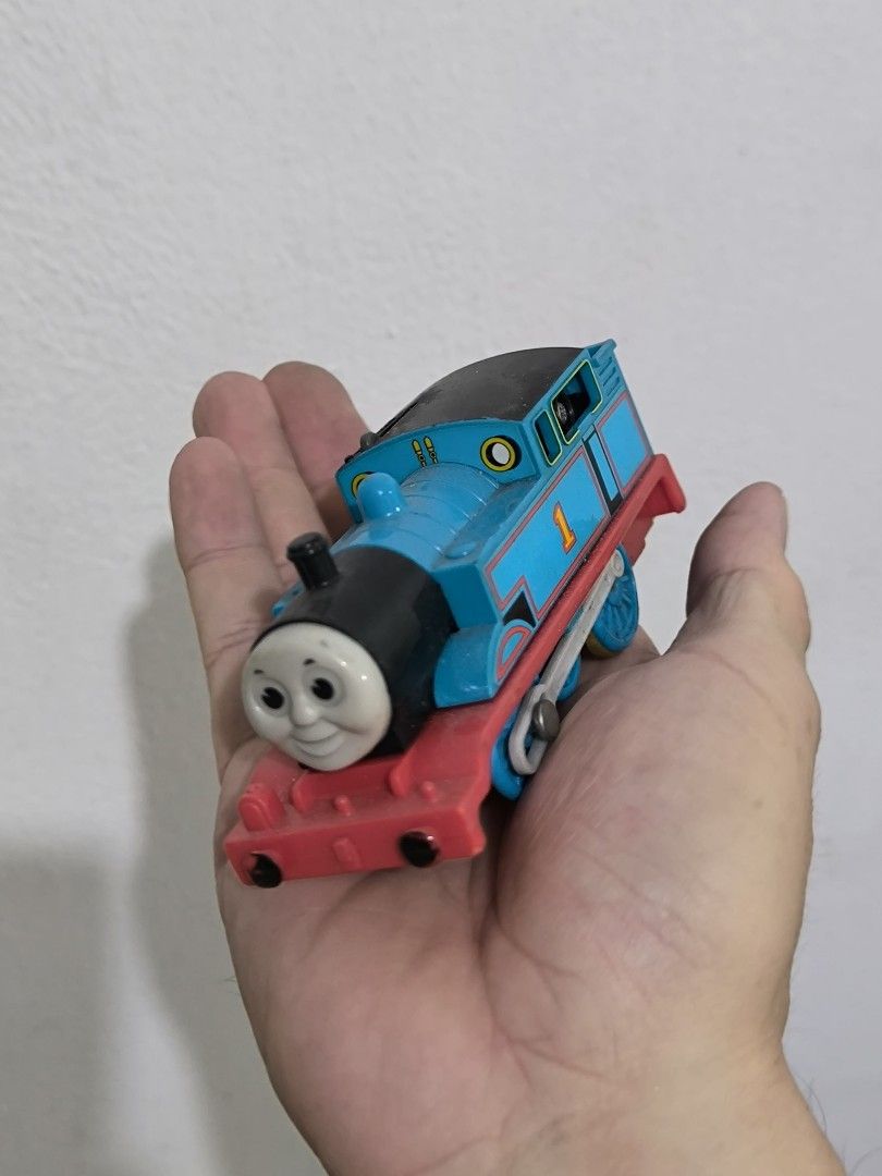 Tomica Thomas the Tank Engine Train (Category: Vehicle & Diecast Models) located in Angeles City. Submitted by yellowbrickstore (Listing ID 1427507933, Image 3). Description: Tomica Thomas the Tank diecast Engine toy train. It is blue with a red base and has the number 1 on its side. The train is made in Thailand. The wheels are blue and yellow. The underside of the train has the Tomica logo and other markings shipping via jnt express sat sked on