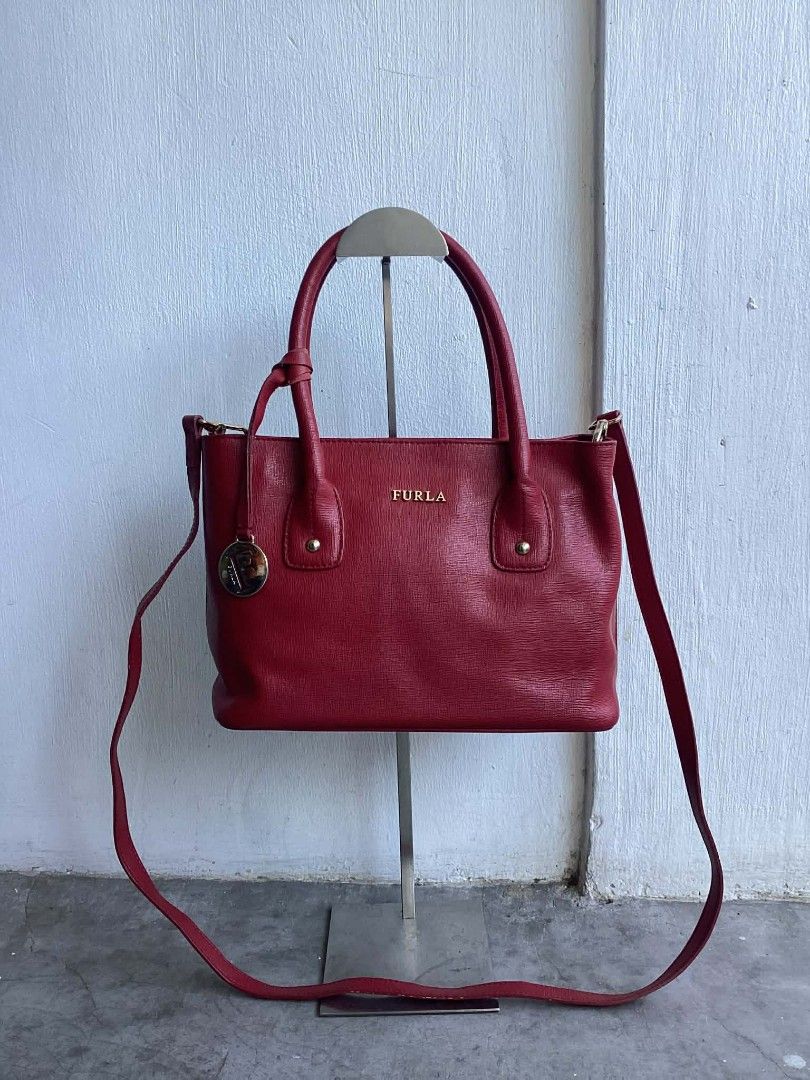 Furla Red Wine Leather Satchel (Category: Luxury Bags & Wallets) located in Cavite. Submitted by benta_bounce (Listing ID 1427698586, Image 2). Description: Furla handbag is made of red leather. It features a top handle and a detachable shoulder strap. The interior has a zipper pocket and a Furla label. The bag has gold-tone hardware and protective feet on the bottom. The Furla logo is visible on the front. Measurements: Width: 34cm Height: 19.5c