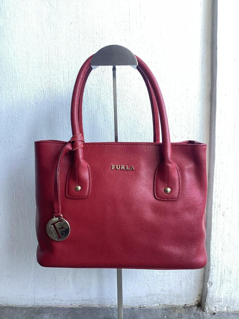 Furla Red Wine Leather Satchel (Category: Luxury Bags & Wallets) located in Cavite. Submitted by benta_bounce (Listing ID 1427698586, Image 1). Description: Furla handbag is made of red leather. It features a top handle and a detachable shoulder strap. The interior has a zipper pocket and a Furla label. The bag has gold-tone hardware and protective feet on the bottom. The Furla logo is visible on the front. Measurements: Width: 34cm Height: 19.5c