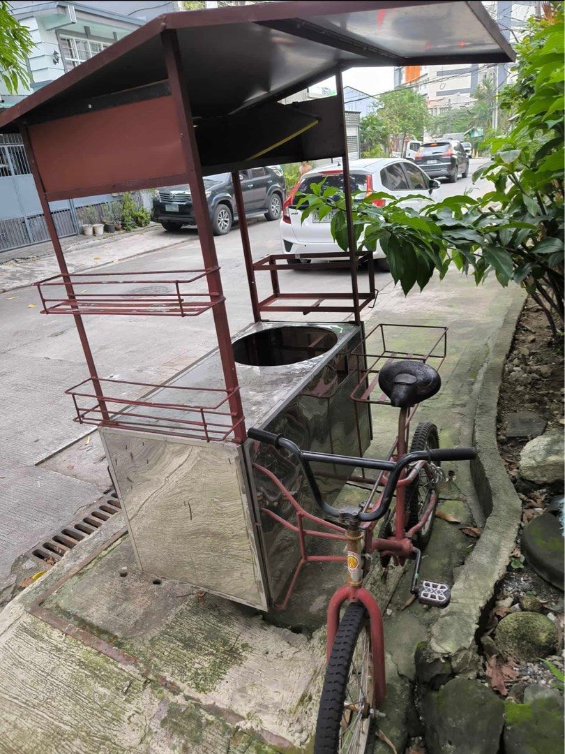 Mobile Food Cart with Bicycle (Category: Bicycles) located in Quezon City. Submitted by klengkerz (Listing ID 1427727749, Image 1). Description: Mobile food cart with a stainless steel body and a built-in cooking area. Features a roof for shade and multiple shelves for display. Includes a bicycle for easy mobility. The cart has a red frame and wheels..