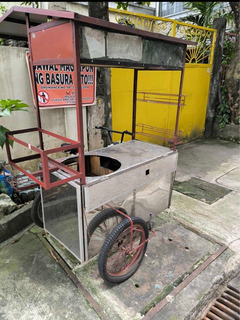Mobile Food Cart with Bicycle (Category: Bicycles) located in Quezon City. Submitted by klengkerz (Listing ID 1427727749, Image 3). Description: Mobile food cart with a stainless steel body and a built-in cooking area. Features a roof for shade and multiple shelves for display. Includes a bicycle for easy mobility. The cart has a red frame and wheels..