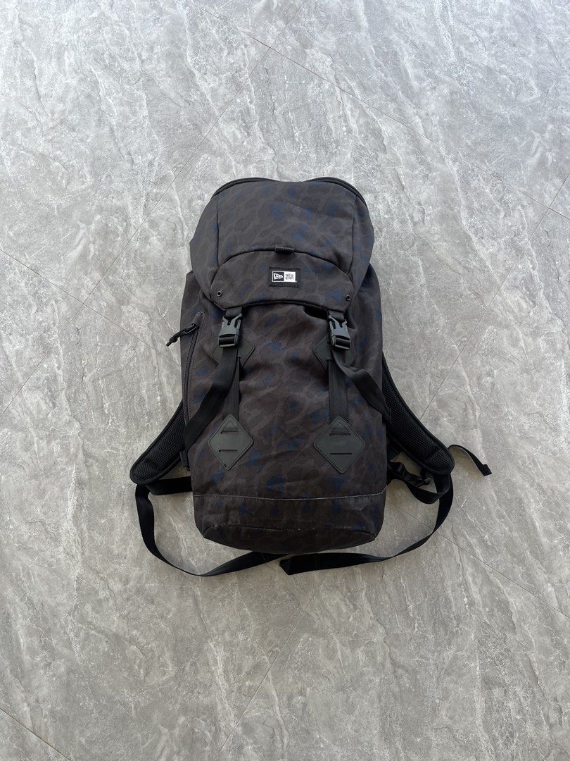New Era Camo Backpack (Category: Backpacks) located in Dagami. Submitted by donsthrift (Listing ID 1427673603, Image 1). Description: New Era backpack features a camouflage pattern. It has adjustable shoulder straps, multiple compartments, and a top handle. The backpack includes a flap closure with buckles and a padded back panel for comfort. It also has the New Era logo on the front and back..