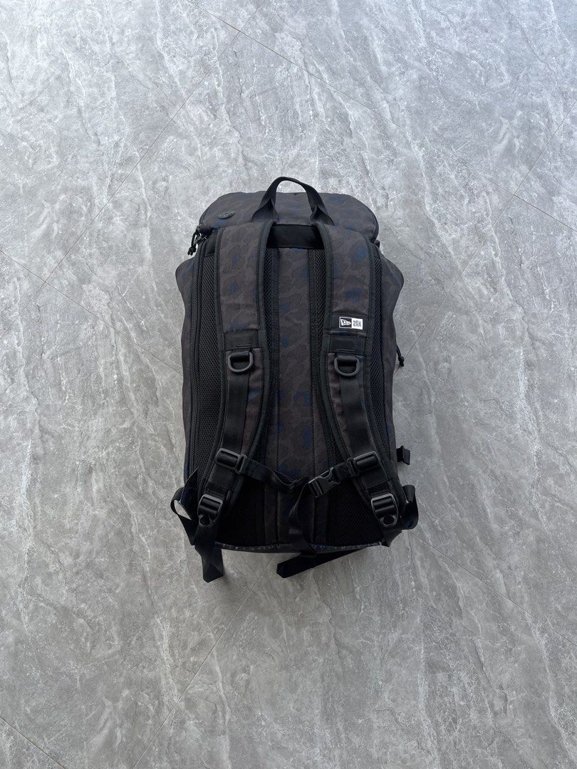 New Era Camo Backpack (Category: Backpacks) located in Dagami. Submitted by donsthrift (Listing ID 1427673603, Image 2). Description: New Era backpack features a camouflage pattern. It has adjustable shoulder straps, multiple compartments, and a top handle. The backpack includes a flap closure with buckles and a padded back panel for comfort. It also has the New Era logo on the front and back..