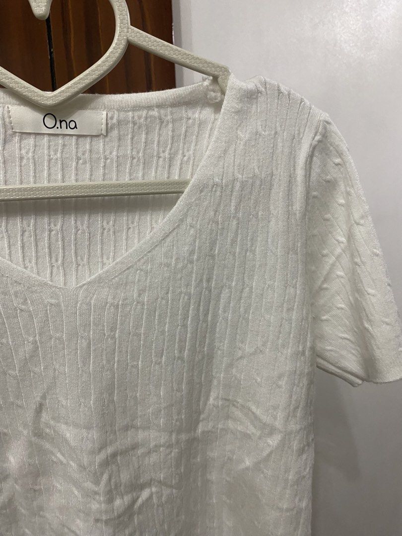 o.na White Cable Knit V-Neck Top (Category: Sleeveless) located in Pateros City. Submitted by downsizin (Listing ID 1427648532, Image 2). Description: White V-neck top from O.na. Features short sleeves and a textured knit design. The top has a simple, elegant style. The label is visible on the inside of the neckline. The top is on a heart-shaped hanger..