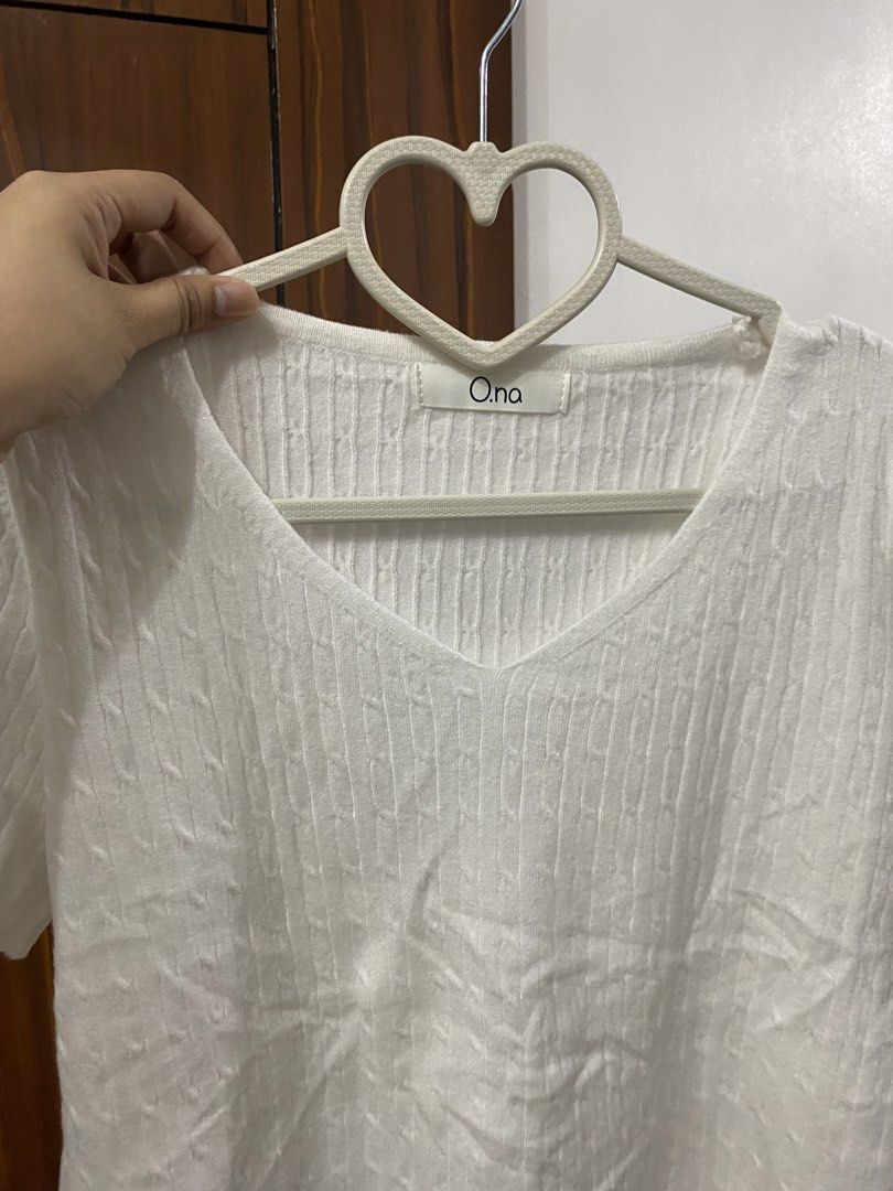 o.na White Cable Knit V-Neck Top (Category: Sleeveless) located in Pateros City. Submitted by downsizin (Listing ID 1427648532, Image 3). Description: White V-neck top from O.na. Features short sleeves and a textured knit design. The top has a simple, elegant style. The label is visible on the inside of the neckline. The top is on a heart-shaped hanger..