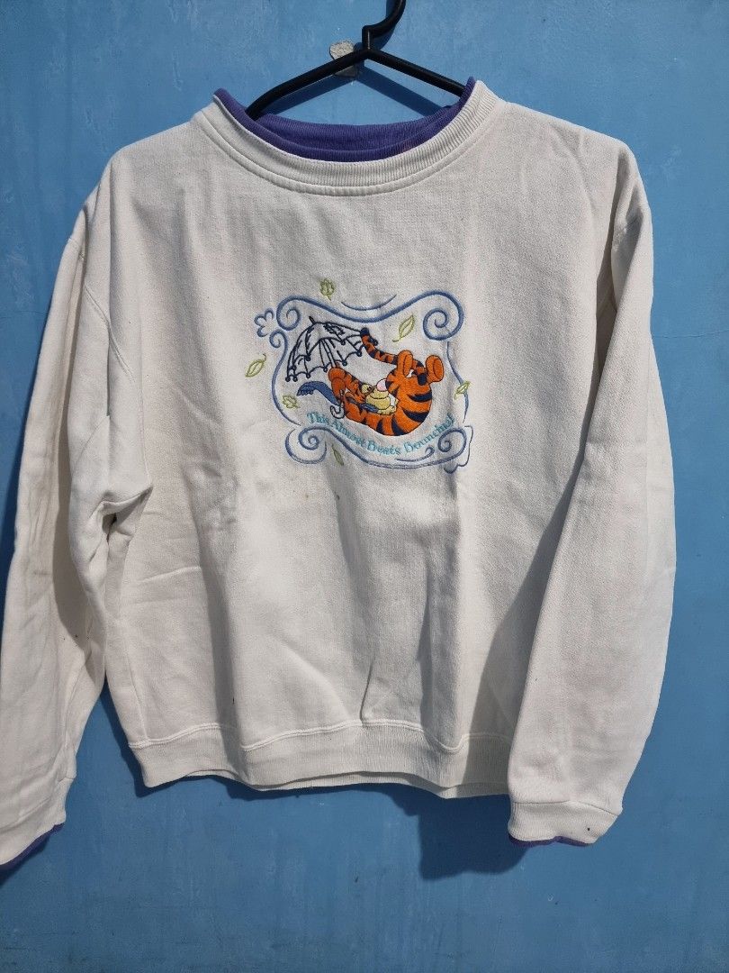 Pooh Tigger Embroidered Sweatshirt L/G (Category: Coats, Jackets and Outerwear) located in Malolos. Submitted by ejaythrift (Listing ID 1427732910, Image 1). Description: Sweatshirt features an embroidered design of Tigger from Winnie the Pooh. It has a purple collar and cuffs. The size is L/G. The sweatshirt is white with a blue and orange design. The Pooh brand tag is visible..