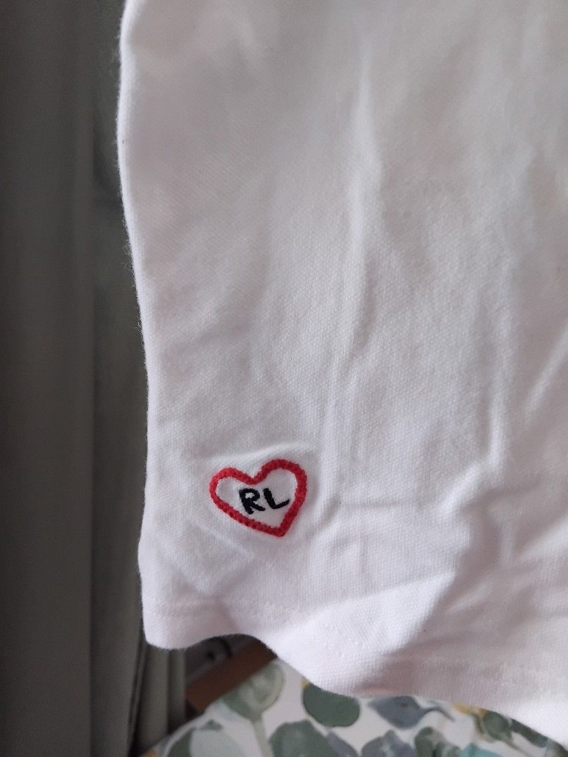 Ralph Lauren White Polo Shirt (Category: Babies & Kids Fashion) located in Manila. Submitted by leontheexplorer (Listing ID 1427697644, Image 3). Description: - White polo shirt from Ralph Lauren - Features a small pink logo on the chest and embroidered details on the sleeve - Includes a heart design with "RL" on the side - Fits up to 6 yrs old depending on the body frame - Has a classic polo collar and button-up front - The shirt is short-sleeve
