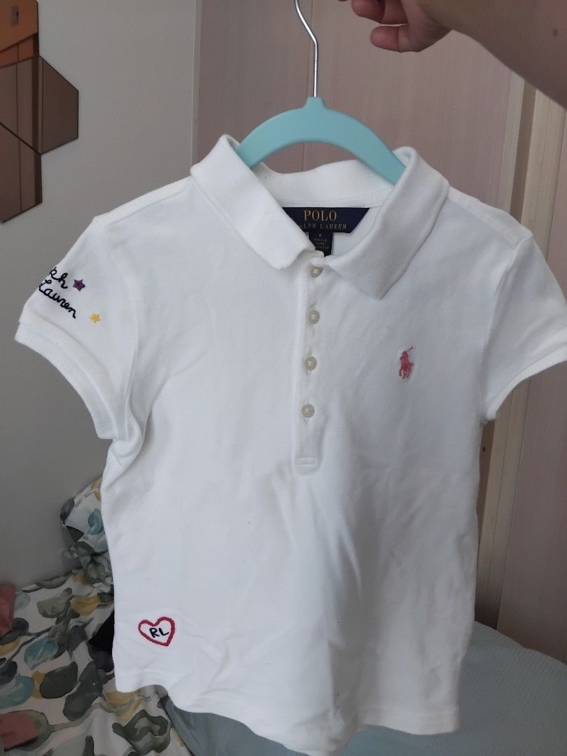 Ralph Lauren White Polo Shirt (Category: Babies & Kids Fashion) located in Manila. Submitted by leontheexplorer (Listing ID 1427697644, Image 1). Description: - White polo shirt from Ralph Lauren - Features a small pink logo on the chest and embroidered details on the sleeve - Includes a heart design with "RL" on the side - Fits up to 6 yrs old depending on the body frame - Has a classic polo collar and button-up front - The shirt is short-sleeve