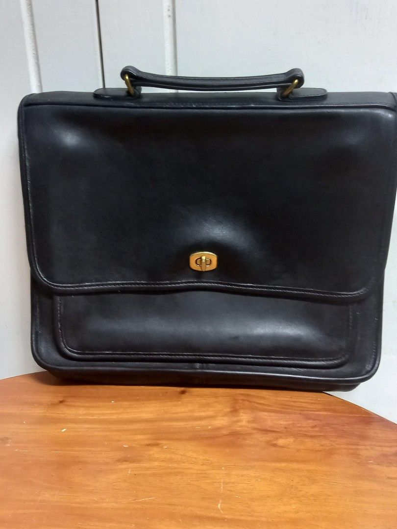 Coach Black Leather Briefcase (Category: Briefcases) located in Tuguegarao City. Submitted by zenphoenix-7ad615 (Listing ID 1427872018, Image 1). Description: Classic Coach briefcase in black leather. Features a flap closure with a gold-tone turn lock. Includes a top handle and a front pocket. The interior has a zipper pocket and a Coach logo. The tag shows the style number 9850. A timeless and stylish accessory for everyday use. 13.5 by 10 inche