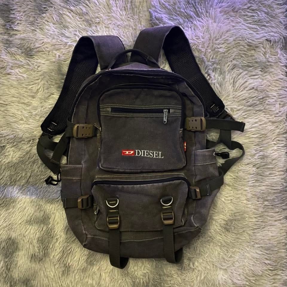 Diesel Canvas Backpack (Negotiable) (Category: Backpacks) located in Manila. Submitted by nevergiveafck (Listing ID 1427822806, Image 1). Description: Durable Diesel backpack in a dark grey canvas. Features multiple pockets, including a front zippered pocket and two smaller front pockets with buckles. Adjustable shoulder straps and a top handle for carrying. The Diesel logo is prominently displayed on the front. Perfect for everyday use..