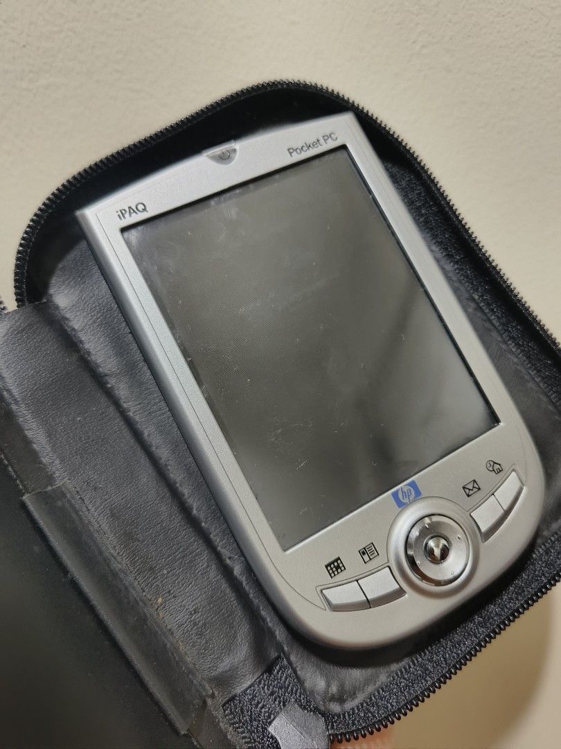 HP iPAQ Pocket PC (Category: Desktops) located in Baguio. Submitted by alk08 (Listing ID 1427901165, Image 1). Description: HP iPAQ Pocket PC with a protective case. The device has a silver finish and features a screen, buttons, and a navigation wheel. It includes a stylus and a battery compartment. The case is black and has a zipper closure..
