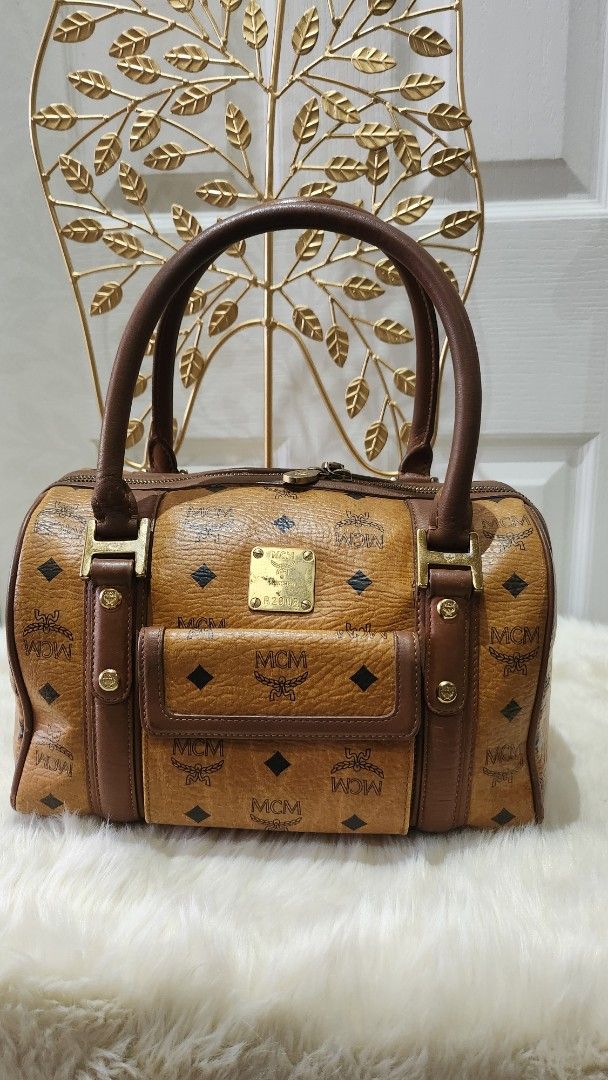 MCM Boston Bag (Category: Luxury Bags & Wallets) located in Cavite. Submitted by geturs (Listing ID 1427803309, Image 1). Description: MCM Boston bag in brown. Features the iconic MCM logo print. Includes top handles and a front pocket. The bag has gold-tone hardware and brown leather trim. A stylish and functional accessory for everyday use..