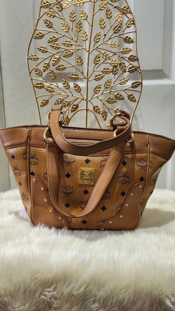 MCM handbag (Category: Luxury Bags & Wallets) located in Cavite. Submitted by geturs (Listing ID 1427803710, Image 2). Description: Authentic MCM Visetos tote bag. Features the iconic MCM logo pattern. The bag has a top handle and a zipper closure. The exterior is brown with gold-tone hardware. A gold MCM logo plate is visible on the front..