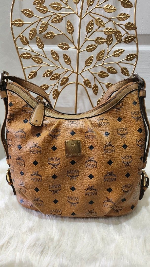 MCM Visetos Shoulder Bag (Category: Luxury Bags & Wallets) located in Cavite. Submitted by geturs (Listing ID 1427802882, Image 2). Description: MCM Visetos shoulder bag in brown. Features the iconic MCM logo pattern. Includes a shoulder strap and a front flap closure with a buckle. The bag has a unique design element on the side with a leaf-like pattern..