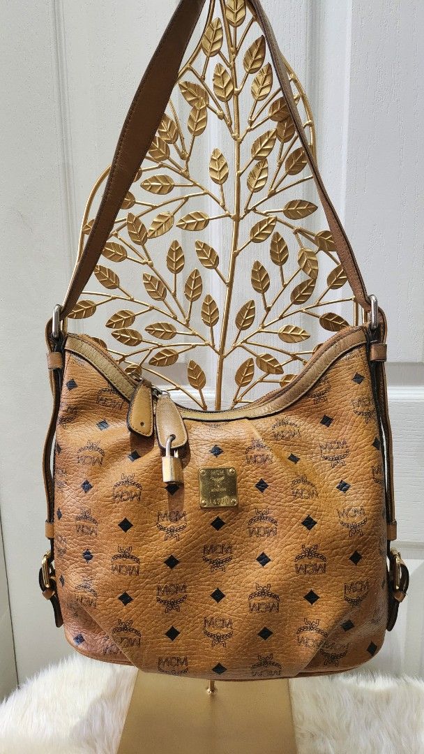 MCM Visetos Shoulder Bag (Category: Luxury Bags & Wallets) located in Cavite. Submitted by geturs (Listing ID 1427802882, Image 1). Description: MCM Visetos shoulder bag in brown. Features the iconic MCM logo pattern. Includes a shoulder strap and a front flap closure with a buckle. The bag has a unique design element on the side with a leaf-like pattern..