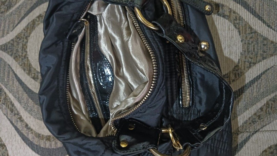 Tod's Black Nylon Handbag (Category: Luxury Bags & Wallets) located in Laoag. Submitted by catrnzjb153008 (Listing ID 1427823626, Image 3). Description: Black nylon handbag from Tod's. Features multiple zippered compartments and gold-toned hardware. The interior lining is a light, silky material. The bag has a shoulder strap with a patent leather accent. The Tod's logo is visible on the zipper and the strap. Includes a small charm with the Tod's 
