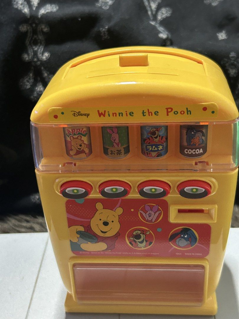 Disney Winnie the Pooh Vending Machine Toy (Category: Character Goods) located in Angeles City. Submitted by zyeplustradings (Listing ID 1428094865, Image 2). Description: Yellow Disney Winnie the Pooh vending machine toy. It features four drink options: Apple, Tea, Ramune, and Cocoa. The toy has buttons and illustrations of Winnie the Pooh and his friends..