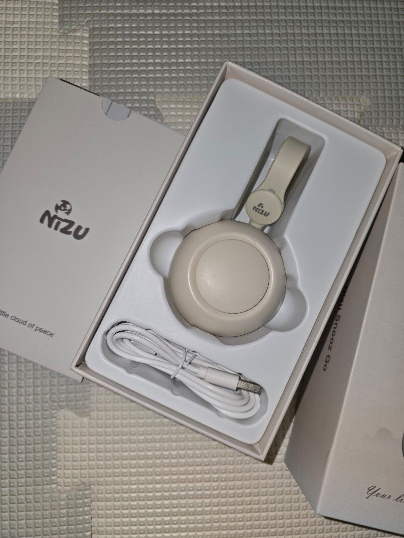NIZU Snooz Go Portable Sound Machine (Category: Soundbars, Speakers & Amplifiers) located in Pasig City. Submitted by momofwillow (Listing ID 1428058994, Image 2). Description: NIZU Snooz Go is a portable sound machine designed to help babies sleep. It comes with a USB charging cable and can be clipped onto strollers, baby carriers, or diaper bags. The device has multiple buttons and a light ring. The packaging includes the device, a charging cab