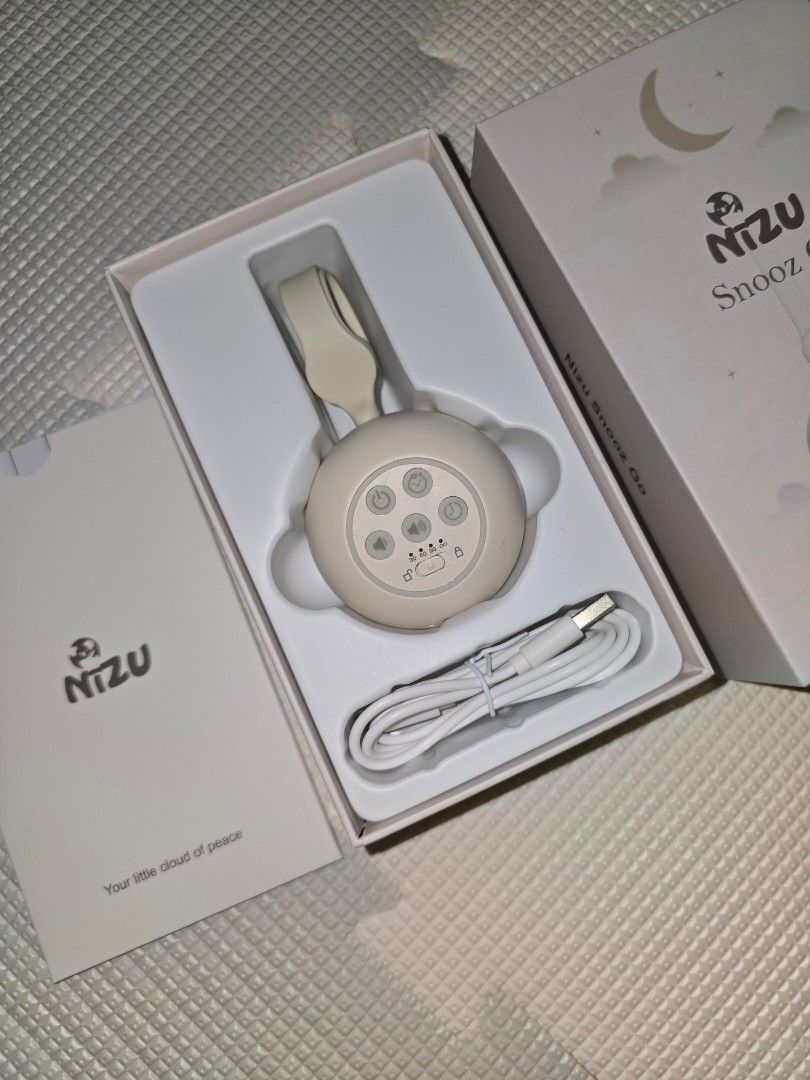 NIZU Snooz Go Portable Sound Machine (Category: Soundbars, Speakers & Amplifiers) located in Pasig City. Submitted by momofwillow (Listing ID 1428058994, Image 3). Description: NIZU Snooz Go is a portable sound machine designed to help babies sleep. It comes with a USB charging cable and can be clipped onto strollers, baby carriers, or diaper bags. The device has multiple buttons and a light ring. The packaging includes the device, a charging cab