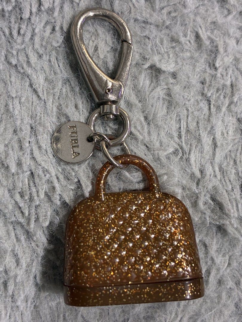 Original Furla Bag Charm Key Chain (Category: Luxury Accessories) located in Manila. Submitted by cellymeji060371 (Listing ID 1427961243, Image 2). Description: Furla key chain features a miniature bag charm with a glittery, brown finish. It has a silver-tone clasp and a Furla logo tag. The charm has a quilted design and a small handle. It's a stylish accessory for your keys or bag. The perfect accessory for your bag❤️ Super cutie😍.