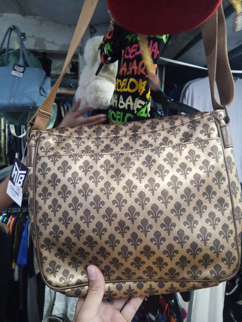 Patrick Cox Shoulder Bag (Category: Luxury Bags & Wallets) located in Lucban. Submitted by aeronroyyy (Listing ID 1428034950, Image 2). Description: Stylish shoulder bag from Patrick Cox. Features a repeating fleur-de-lis pattern in brown and gold. Includes a long shoulder strap. The bag has a rectangular shape with a front pocket. The interior lining is brown. The Patrick Cox brand label is visible inside the bag..