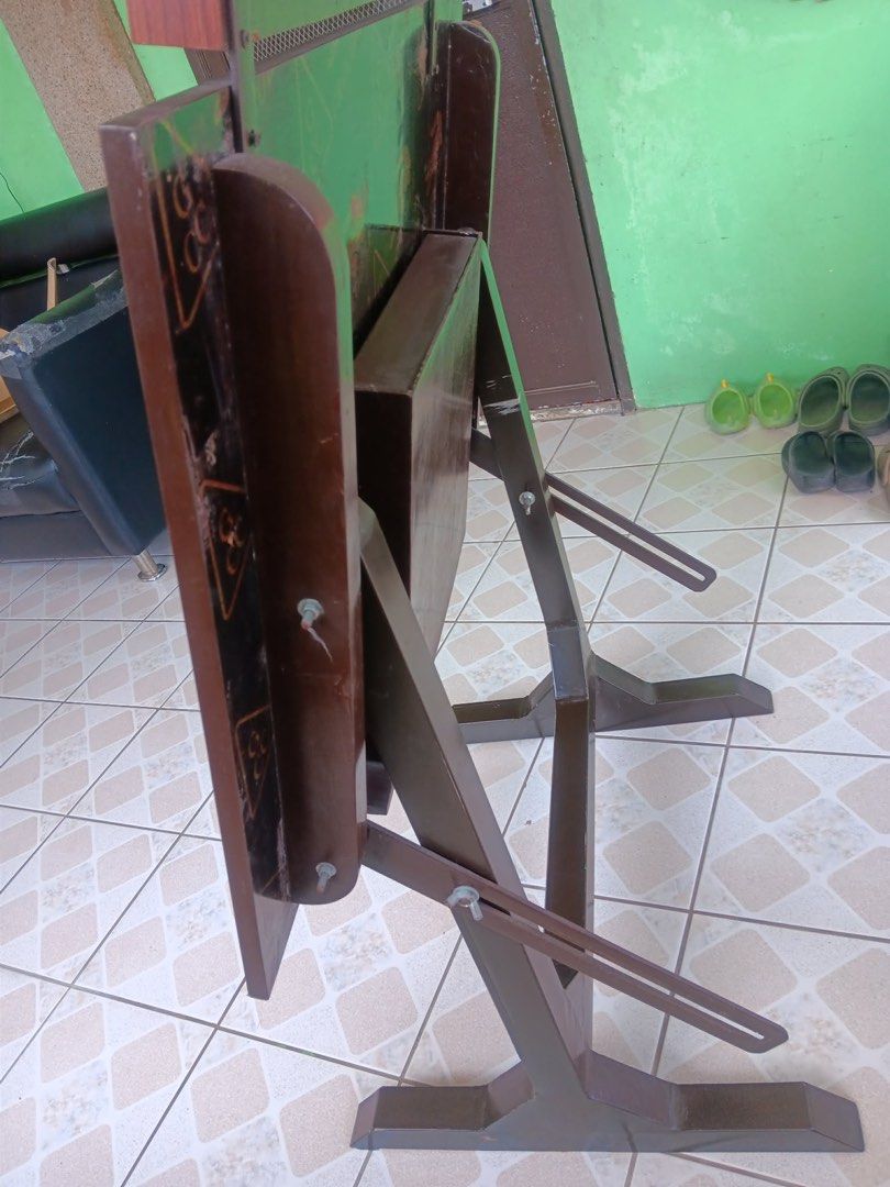 Wooden Drafting Table with Storage (Category: Tables & Sets) located in Pasig City. Submitted by khiarha (Listing ID 1427985217, Image 3). Description: Wooden drafting table features a dark wood finish and a built-in storage compartment. It has a slatted top section and a section with multiple circular holes. The table is supported by a sturdy metal frame. The table's surface has a wood grain pattern. The table also has a storage area underneath 