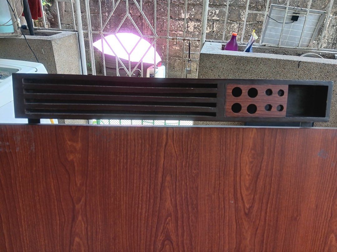 Wooden Drafting Table with Storage (Category: Tables & Sets) located in Pasig City. Submitted by khiarha (Listing ID 1427985217, Image 1). Description: Wooden drafting table features a dark wood finish and a built-in storage compartment. It has a slatted top section and a section with multiple circular holes. The table is supported by a sturdy metal frame. The table's surface has a wood grain pattern. The table also has a storage area underneath 
