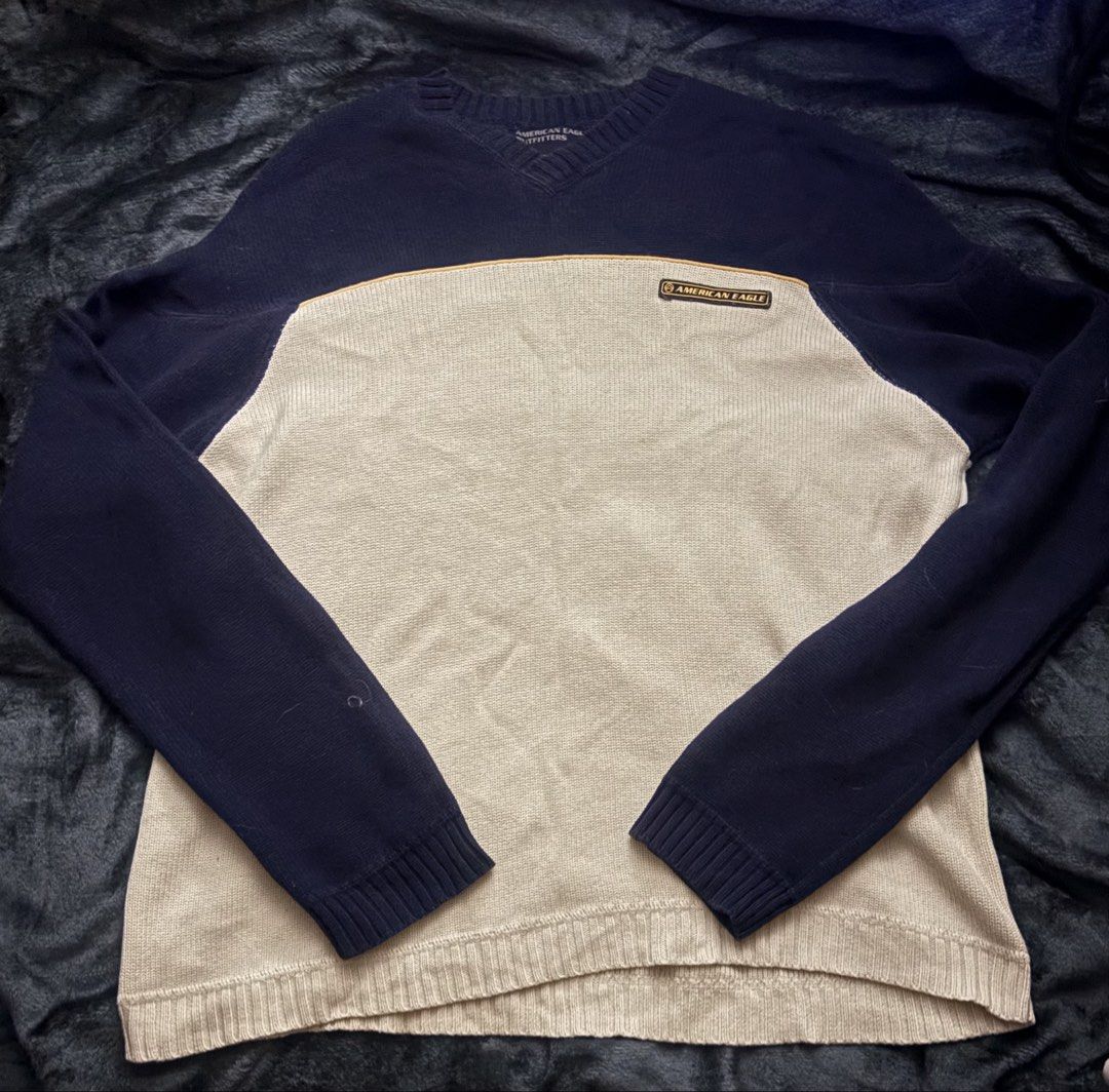 American Eagle V-Neck Sweater (Category: Coats, Jackets and Outerwear) located in Manila. Submitted by isha0629 (Listing ID 1428126291, Image 1). Description: American Eagle V-neck sweater. Features a beige body with navy blue sleeves and neckline. Includes a small logo patch on the chest. Ribbed cuffs and hem. A small imperfection is visible on the left sleeve. Perfect for casual wear..