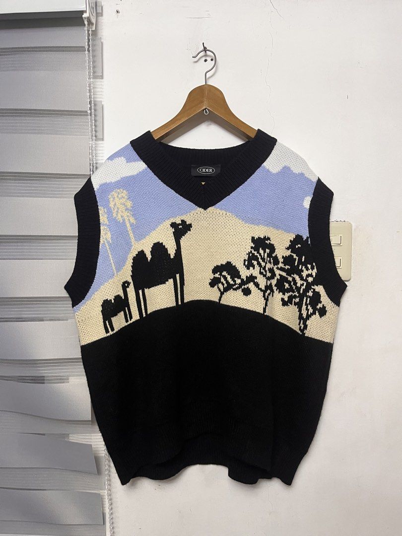 Cider Camel Graphic Vest - Size L (Category: Vests) located in Cabuyao City. Submitted by kisyana (Listing ID 1428251906, Image 1). Description: Cider vest featuring a camel graphic design. It has a V-neck and a black base. The vest is size L. The design includes a desert scene with camels, trees, and a blue sky. The brand name is visible on the inner tag..