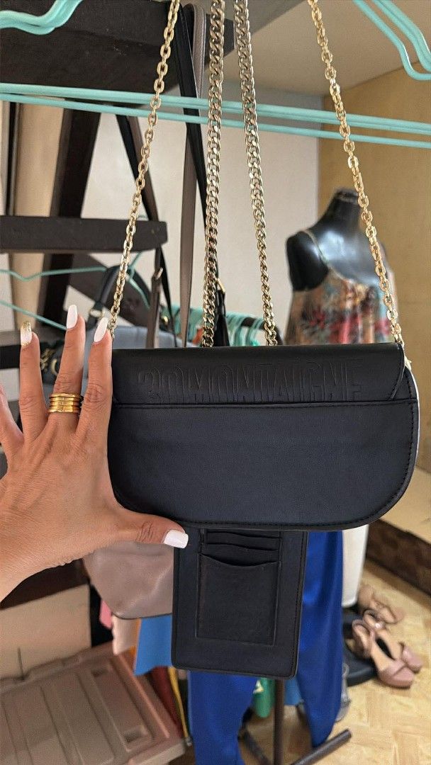 Dior Black Shoulder Bag with Gold Chain (Category: Luxury Bags & Wallets) located in Quezon City. Submitted by rolenalma (Listing ID 1428206802, Image 3). Description: Dior Bobby East - West bag. Elegant black shoulder bag featuring a gold chain strap and a gold-tone CD logo on the front. The bag has a flap closure with a buckle. The back of the bag has a subtle embossed pattern. A small pocket is visible on the back..