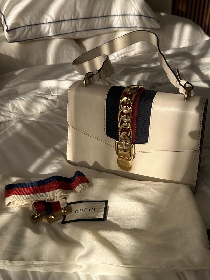 Gucci Sylvie Small Shoulder Bag (Authenticated by LegitGrails) (Category: Luxury Bags & Wallets) located in Manila. Submitted by kristineliban (Listing ID 1403645572, Image 1). Description: RFS: Need funds for home construction project With certificate of authenticity from LegitGrails Gucci Sylvie Small Shoulder Bag features a cream-colored leather exterior with a gold-tone chain and buckle closure. It has a signature red and navy stripe detail o