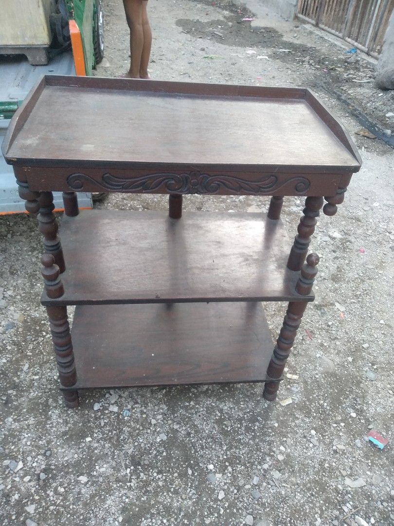Wooden Side Table with Shelves (Category: Tables & Sets) located in Agdangan. Submitted by marymoore (Listing ID 1428171893, Image 1). Description: Wooden side table features a classic design with three tiers for storage. The top shelf has a raised edge, and the legs have a decorative turned design. It's a practical piece for displaying items or serving as a small side table. The table has a dark brown finish..