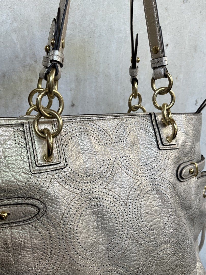 Coach Metallic Silver Tote Bag (Category: Luxury Bags & Wallets) located in Panglao. Submitted by ag.prelovedbags (Listing ID 1428333687, Image 3). Description: Coach tote bag in metallic silver. Features a zip closure, side pockets with drawstring, and gold-tone hardware. Includes a Coach hangtag. The interior has a light purple lining and a zippered pocket. The bag has a textured finish and a chain detail on the straps..