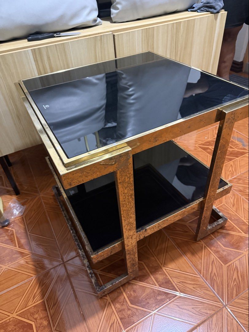 Gold Frame Side Table with Black Glass (Category: Tables & Sets) located in Makati City. Submitted by rctrading (Listing ID 1428427672, Image 3). Description: Stylish side table featuring a gold-colored metal frame and two black glass surfaces. The table has a square shape with a lower shelf for additional storage or display. It's a modern piece that would complement various interior styles. Perfect for living rooms or bedrooms..
