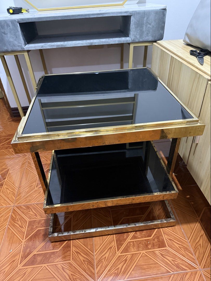 Gold Frame Side Table with Black Glass (Category: Tables & Sets) located in Makati City. Submitted by rctrading (Listing ID 1428427672, Image 1). Description: Stylish side table featuring a gold-colored metal frame and two black glass surfaces. The table has a square shape with a lower shelf for additional storage or display. It's a modern piece that would complement various interior styles. Perfect for living rooms or bedrooms..