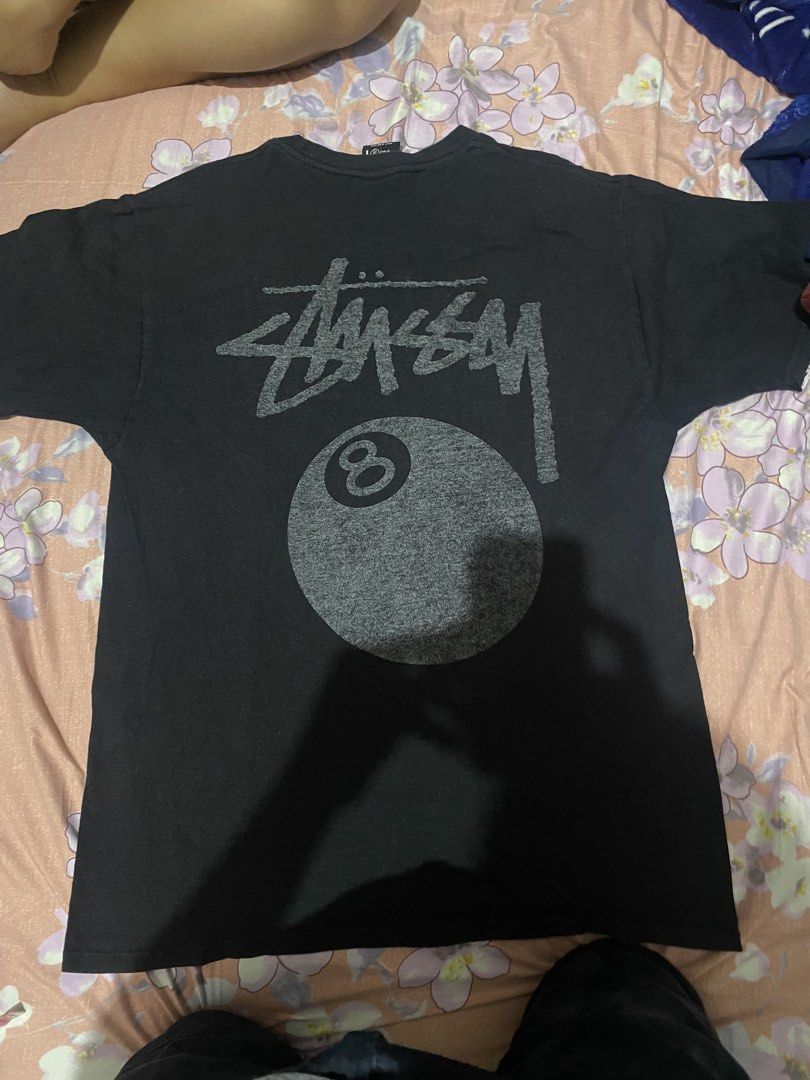 Stussy 8 Ball Graphic Tee (Category: Tshirts & Polo Shirts ) located in Batangas. Submitted by aidenbotchog (Listing ID 1428303188, Image 1). Description: Black Stussy t-shirt featuring the iconic 8 ball graphic on the back. The shirt has a crew neck and short sleeves. The tag indicates it is made of 100% cotton. The size is M. The shirt has the Stussy logo on the front. L29 W19.