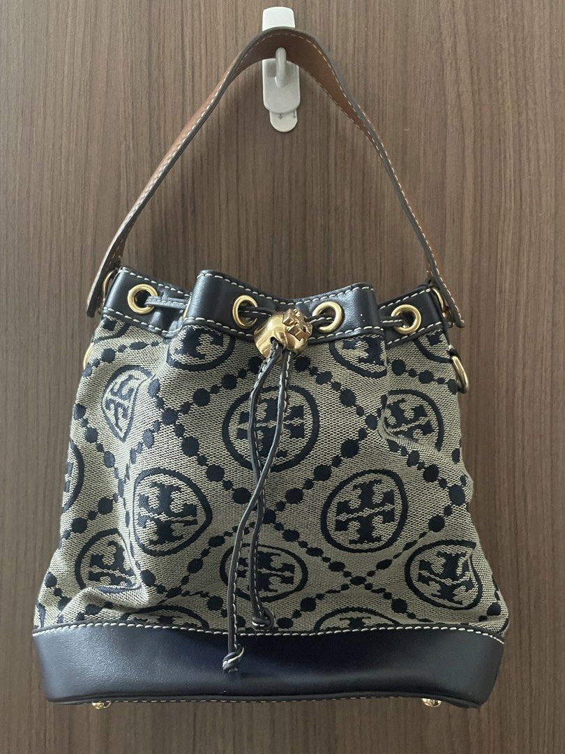 Tory Burch Bucket Bag (Category: Luxury Bags & Wallets) located in Manila. Submitted by misyeli (Listing ID 1428290779, Image 1). Description: Tory Burch bucket bag features a black and beige monogram pattern with a black leather pocket. It has a drawstring closure and a brown leather handle. The interior is yellow with a Tory Burch logo. The bag has gold-tone hardware. There is a small issue on the exterior ( loose stiching) and interior (some s