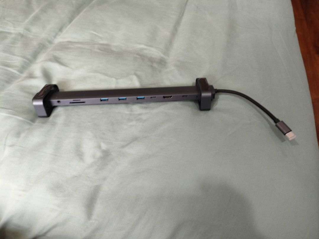 USB-C Hub with Phone Stand (Category: Other Mobile & Gadget Accessories) located in Quezon City. Submitted by alvinkurtgo (Listing ID 1428378851, Image 3). Description: USB-C hub with multiple ports, including USB 3.0, USB-C, and SD card reader. It has a sleek, dark gray design. The hub also comes with a phone stand. The stand is black and has a circular base. The hub connects to devices via a USB-C cable..