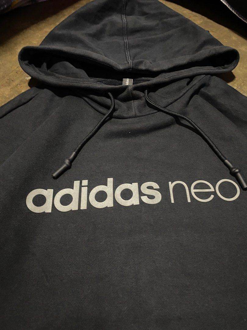 Adidas Neo Hoodie Black (Category: Hoodies) located in Malabon City. Submitted by yivsthrift (Listing ID 1428547832, Image 2). Description: Black Adidas Neo hoodie. Features a hood with drawstrings and a kangaroo pocket. The Adidas Neo logo is printed on the front. The size is A/XL, made in China. The care label is visible, with washing instructions. The hoodie is black. Dimes L31 x W23 inches.