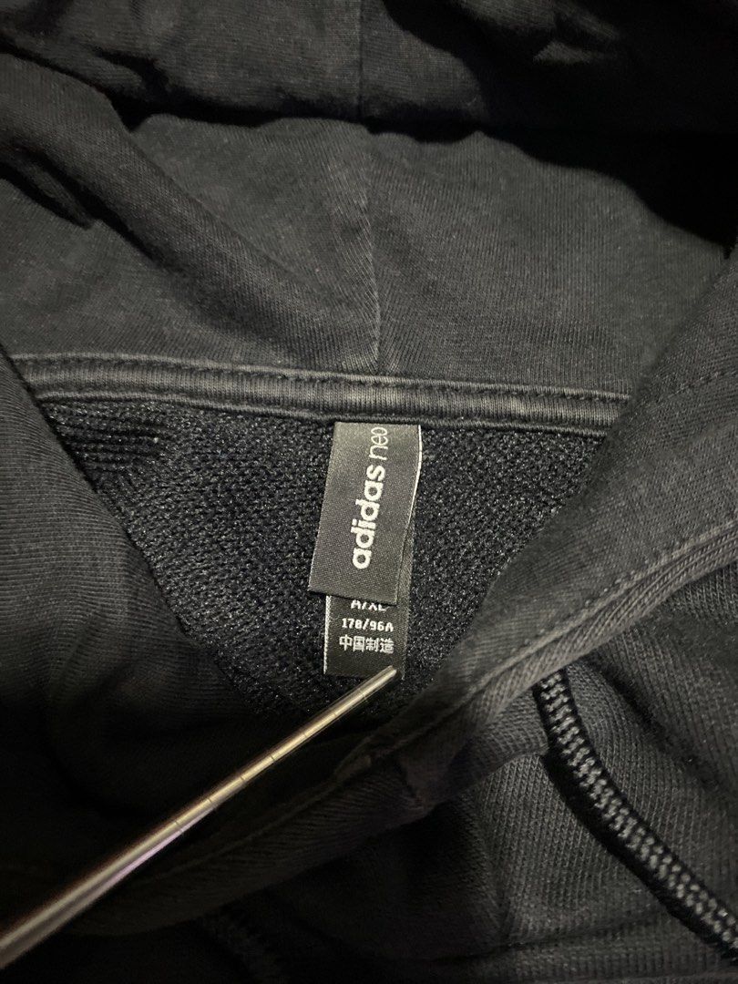 Adidas Neo Hoodie Black (Category: Hoodies) located in Malabon City. Submitted by yivsthrift (Listing ID 1428547832, Image 3). Description: Black Adidas Neo hoodie. Features a hood with drawstrings and a kangaroo pocket. The Adidas Neo logo is printed on the front. The size is A/XL, made in China. The care label is visible, with washing instructions. The hoodie is black. Dimes L31 x W23 inches.