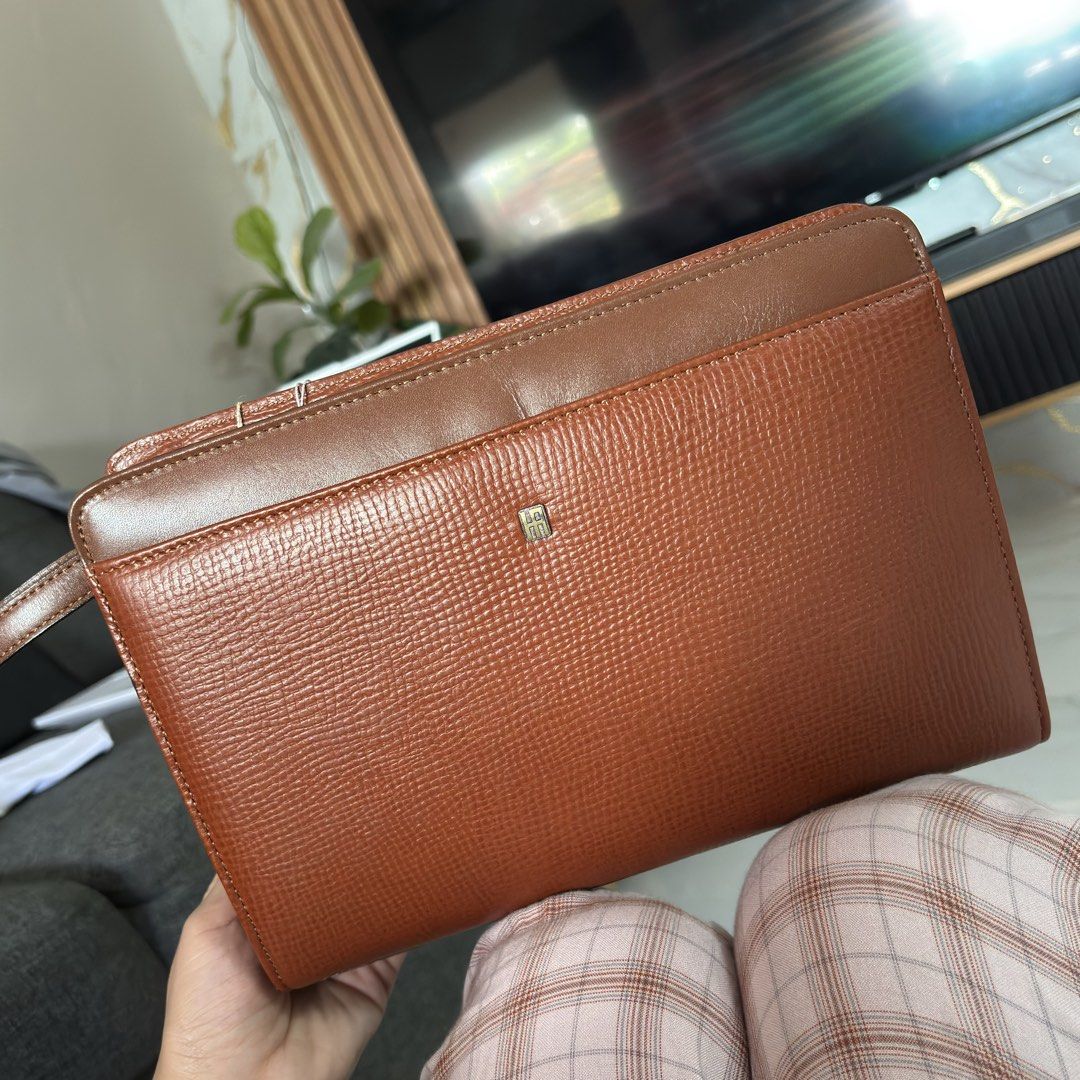 Hardy Amies London Clutch (Category: Clutches) located in Rizal. Submitted by chibibooh (Listing ID 1428474097, Image 1). Description: Authentic Dims 26x19x6 Pwede i-hide yung wrist strap Brown leather clutch from Hardy Amies London. Features a top handle and a zip closure. Includes original tags and paperwork. The interior has multiple compartments. The zipper is marked with YKK. The clutch has a textured exterior and a small logo on the front. 