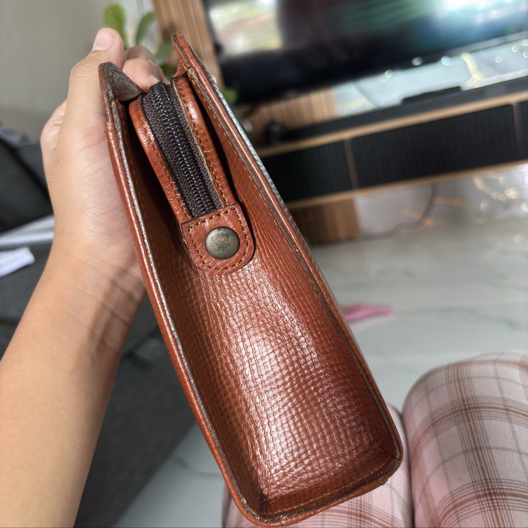 Hardy Amies London Clutch (Category: Clutches) located in Rizal. Submitted by chibibooh (Listing ID 1428474097, Image 3). Description: Authentic Dims 26x19x6 Pwede i-hide yung wrist strap Brown leather clutch from Hardy Amies London. Features a top handle and a zip closure. Includes original tags and paperwork. The interior has multiple compartments. The zipper is marked with YKK. The clutch has a textured exterior and a small logo on the front. 