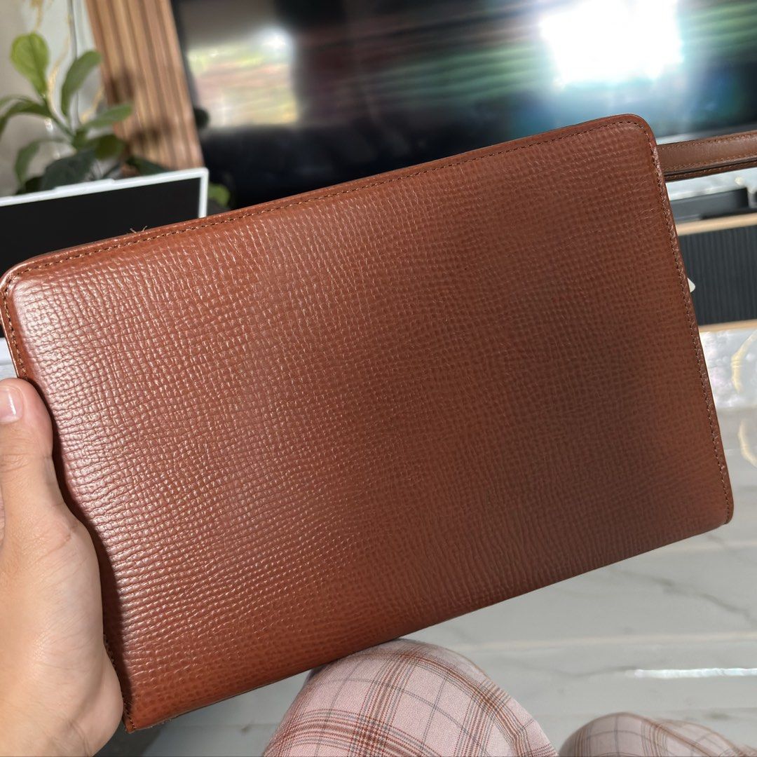 Hardy Amies London Clutch (Category: Clutches) located in Rizal. Submitted by chibibooh (Listing ID 1428474097, Image 2). Description: Authentic Dims 26x19x6 Pwede i-hide yung wrist strap Brown leather clutch from Hardy Amies London. Features a top handle and a zip closure. Includes original tags and paperwork. The interior has multiple compartments. The zipper is marked with YKK. The clutch has a textured exterior and a small logo on the front. 