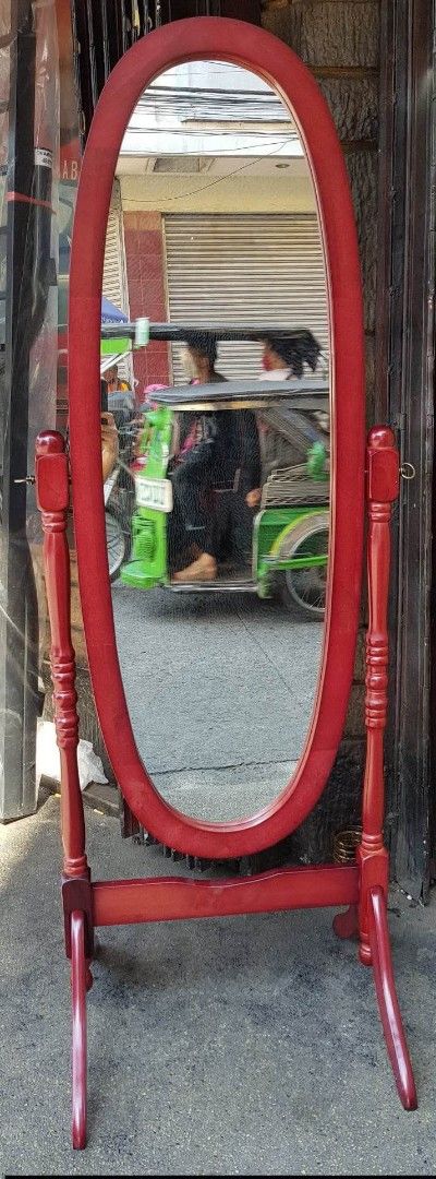 Oval Standing Mirror (Category: Mirrors) located in Manila. Submitted by yzcartph (Listing ID 1428434653, Image 2). Description: Elegant oval-shaped standing mirror with a rich red frame. Features a sturdy wooden stand for stability. Perfect for bedrooms or dressing areas. The mirror provides a full-length view. It is a stylish addition to any space. The frame has a classic design..