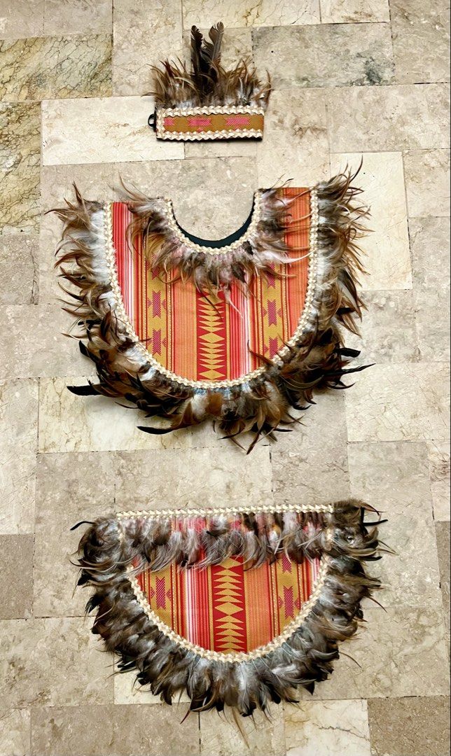 Ati-atihan Costume Set with Feathers (Category: Sets or Coordinates) located in Quezon City. Submitted by clicked.picks (Listing ID 1428733895, Image 1). Description: Ati-atihan costume set includes a headpiece, a top, and a bottom piece, all adorned with feathers. The pieces feature a vibrant red and gold patterned fabric. The edges are trimmed with a cream-colored border..