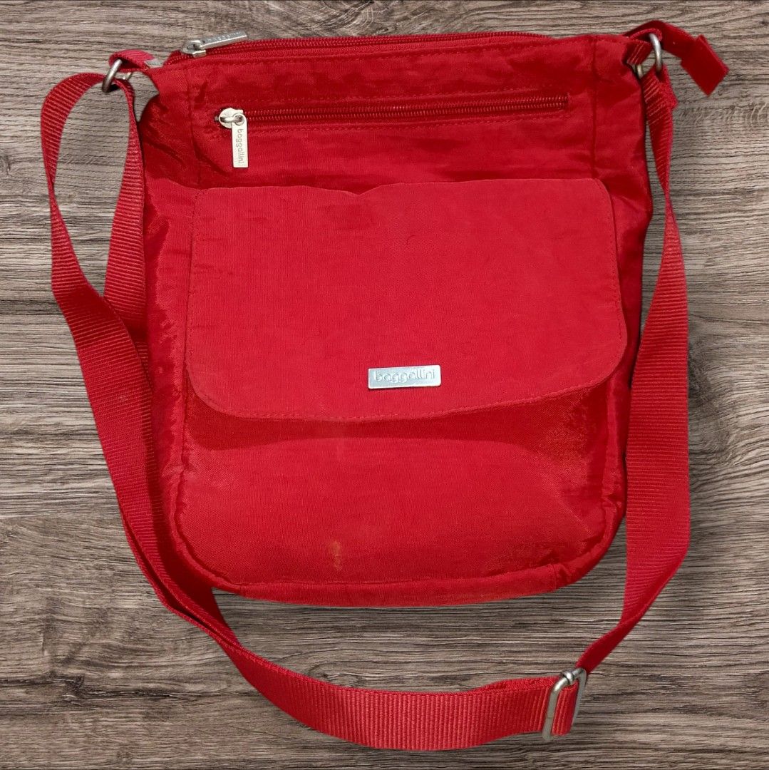 Auth Baggallini Red Nylon Crossbody Bag (Category: Cross-body Bags) located in Cebu City. Submitted by jc_online_shop (Listing ID 1428613962, Image 1). Description: Red Baggallini crossbody bag features a main compartment with a zipper closure and multiple interior pockets. It has an adjustable shoulder strap and an exterior pocket with a magnetic snap closure. The bag's interior is lined with a gray fabric. The bag has a small stain on the front