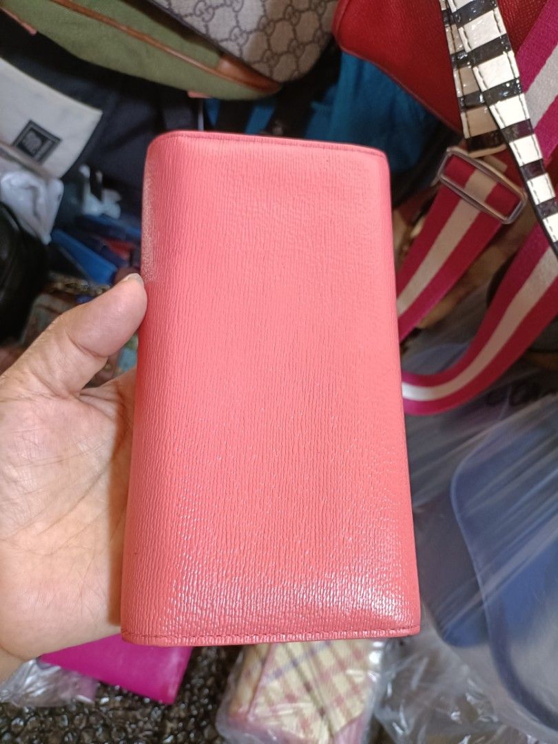 DAKS Coral Pink Long Wallet (Category: Wallets & Card holders) located in Bulacan. Submitted by dstore4u (Listing ID 1428700924, Image 2). Description: Coral pink DAKS long wallet. Features a gold-tone clasp and logo detail. The interior has multiple card slots, a zippered compartment, and a clear ID window. The interior lining is a light beige color. Second hand in good condition .