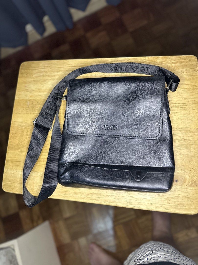 Prada Black Messenger Bag (Category: Luxury Bags & Wallets) located in Cainta. Submitted by mark.silva (Listing ID 1428781892, Image 1). Description: Black messenger bag with a flap closure. Features a Prada logo on the front. The bag has a shoulder strap with the brand name on it. The interior has a zippered pocket..